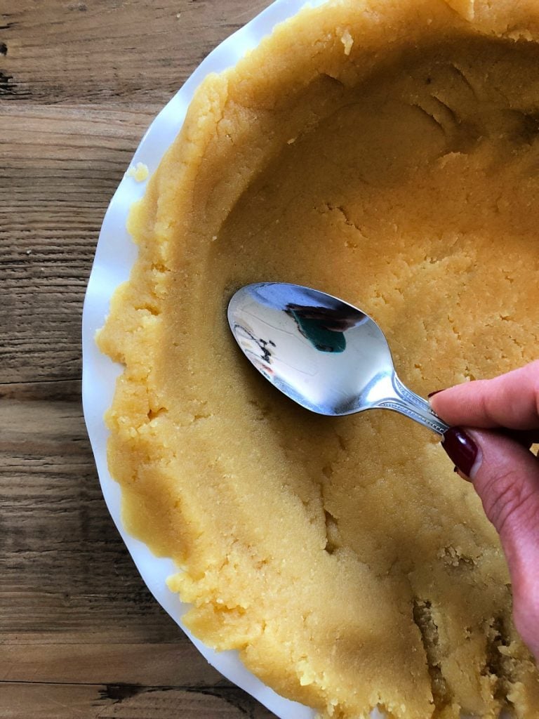 A spoon is pressing down on an Almond Flour crust Pie Plate