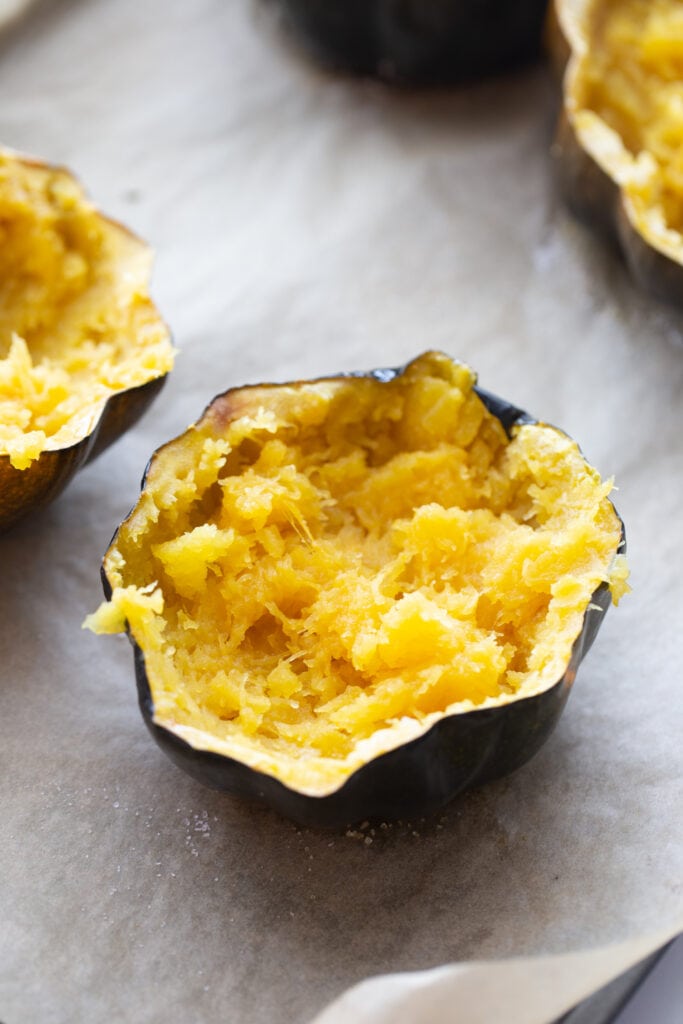 Mashed acorn squash halves, after being roasted in the oven, and ready to be stuffed on a parchment lined baking sheet.