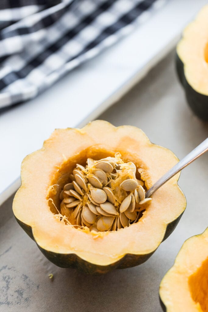 Acorn squash cut in half with a spoon ready to scoop out the seeds of the squash before roasting it in the oven.