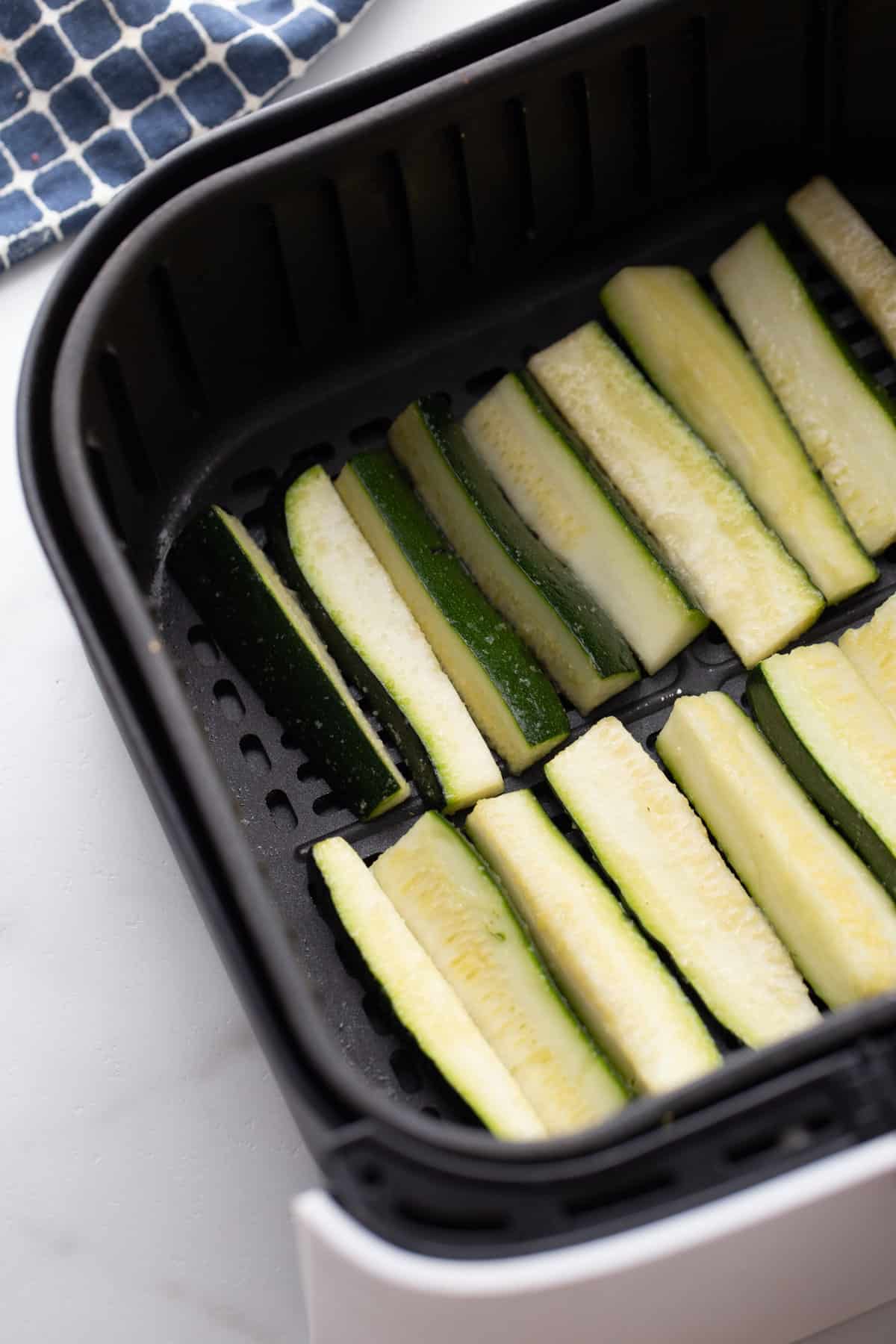 Zucchini cut into fry shapes inside of an air fryer