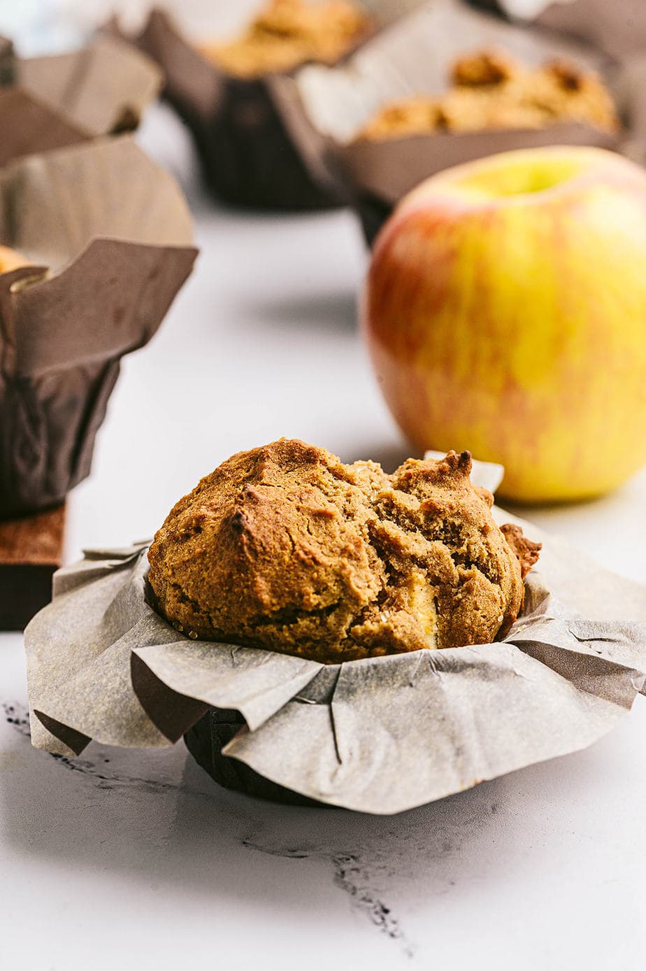 Side view: Healthy apple muffin wrapped in parchment, with many muffins in the background