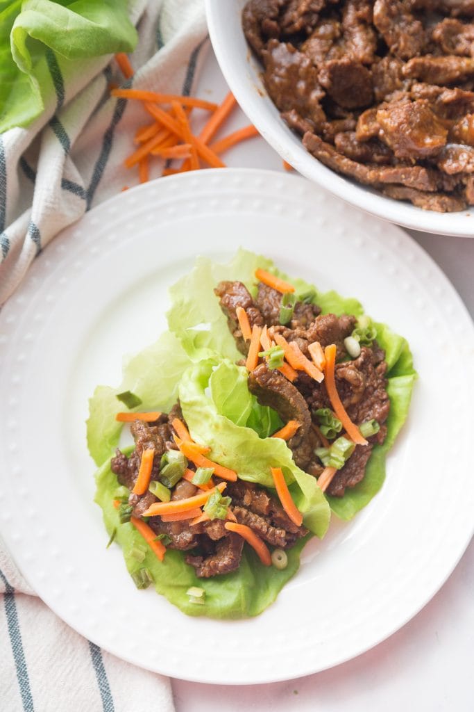 white plate with asian steak two lettuce wraps topped with matchstick carrots. 