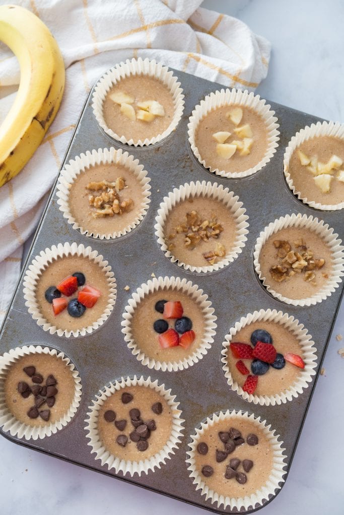A cupcake tray lined with Healthy Blender Oatmeal Muffins with various toppings 
