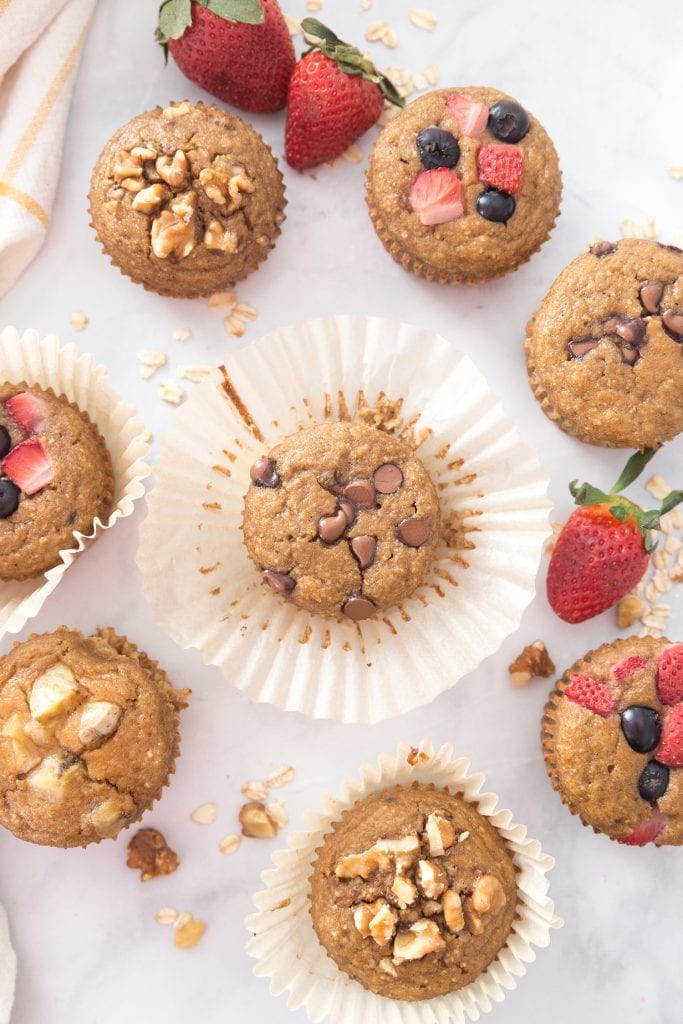 Banana Oatmeal Blender Muffins sitting on a white background topped with chocolate chips, nuts, and berries 