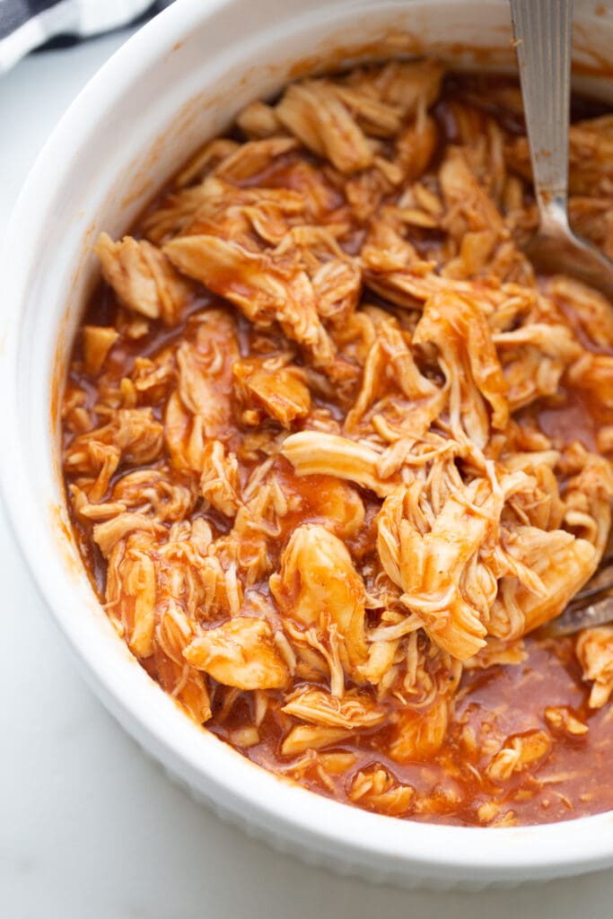 Overhead photo of pulled BBQ chicken in a white casserole dish, fresh from the Instant Pot with a spoon, ready to serve.