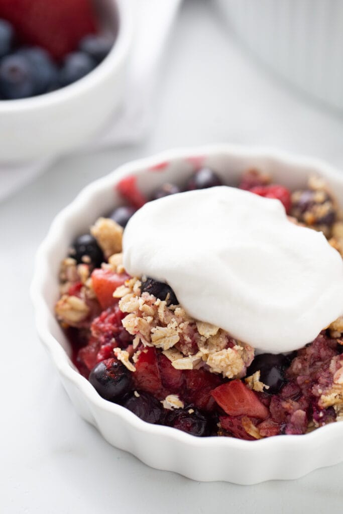 Close up photo of an individual mixed berry crisp topped with homemade coconut cream.