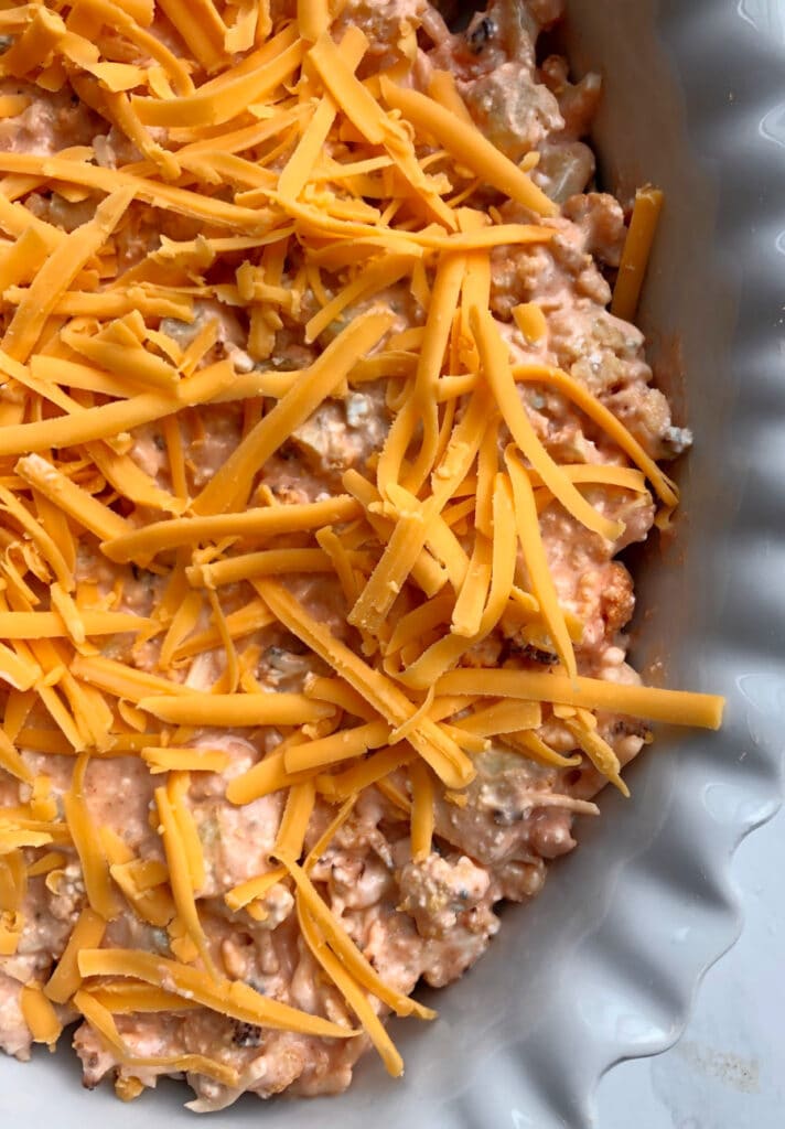 Close up photo of buffalo cauliflower dip topped with shredded cheddar, ready for the oven