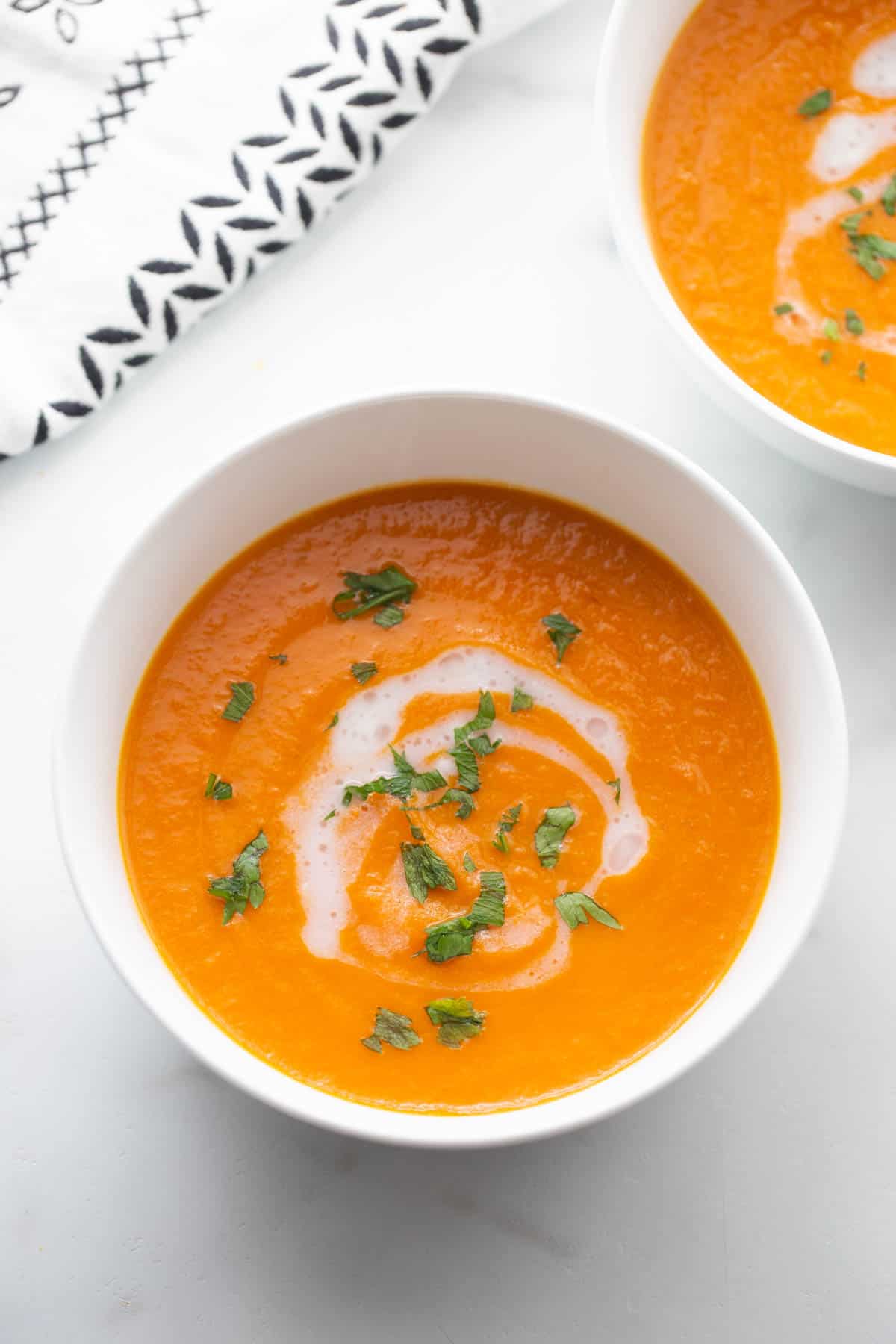 Two bowls of carrot ginger soup with a drizzle of coconut milk and a garnish of fresh parsley. 