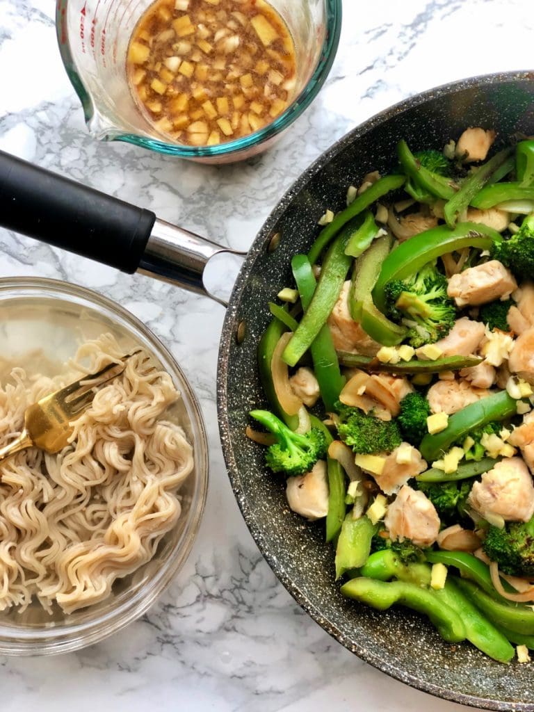 Brown Rice Ramen noodles sitting next to a skillet of chicken and veggies. 