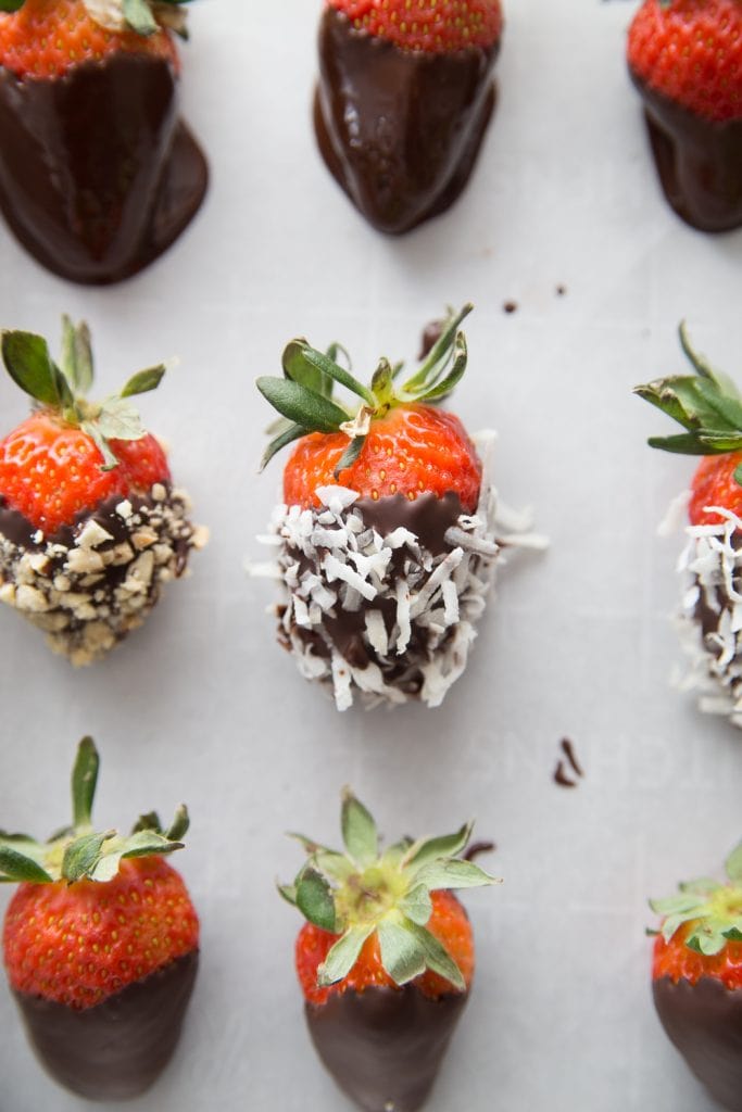 A lined baking sheet with chocolate covered strawberries - some with shredded coconut and some with chopped peanuts