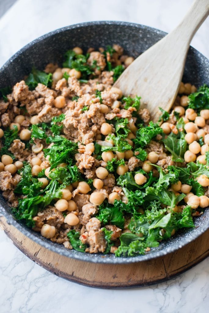 A Skillet is shown with italian chicken sausage, chick peas, and kale. 