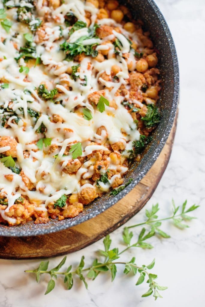 Healthy sausage bean and kale skillet topped with cheese sitting on a marble background. 