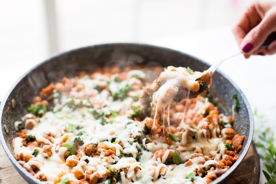 A warm from the stove photo of 21 Day Fix Sausage Bean and Kale Skillet topped with mozzarella cheese. 