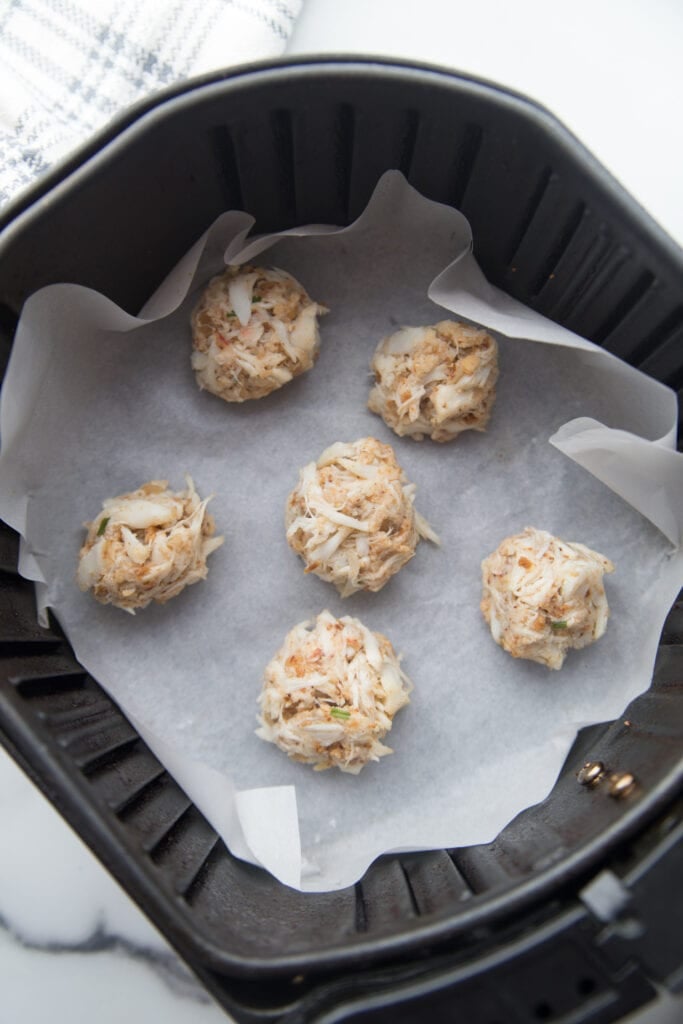 An air fryer basket lined with parchment paper with mini crab cakes