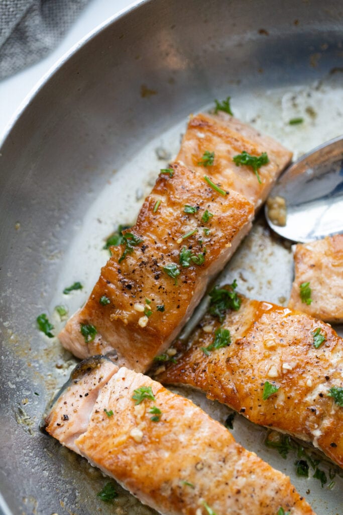 Crispy salmon finished with butter and garlic sauce in a stainless pan