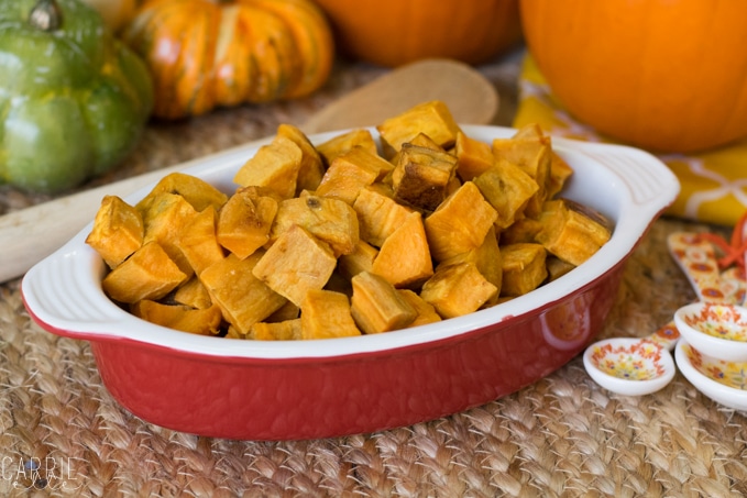 Savory diced sweet potatoes in a red ceramic serving dish with pumpkins in the background