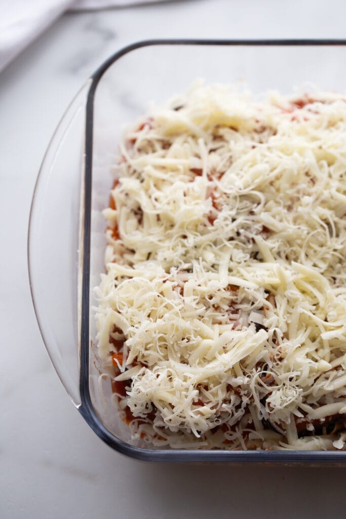 Parmesan and mozzarella cheese cover an uncooked eggplant dish.