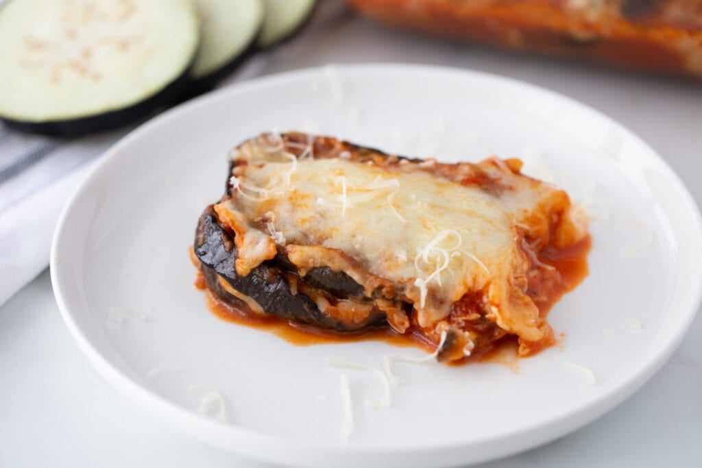 A serving of cheesy eggplant parm is presented on a white plate.