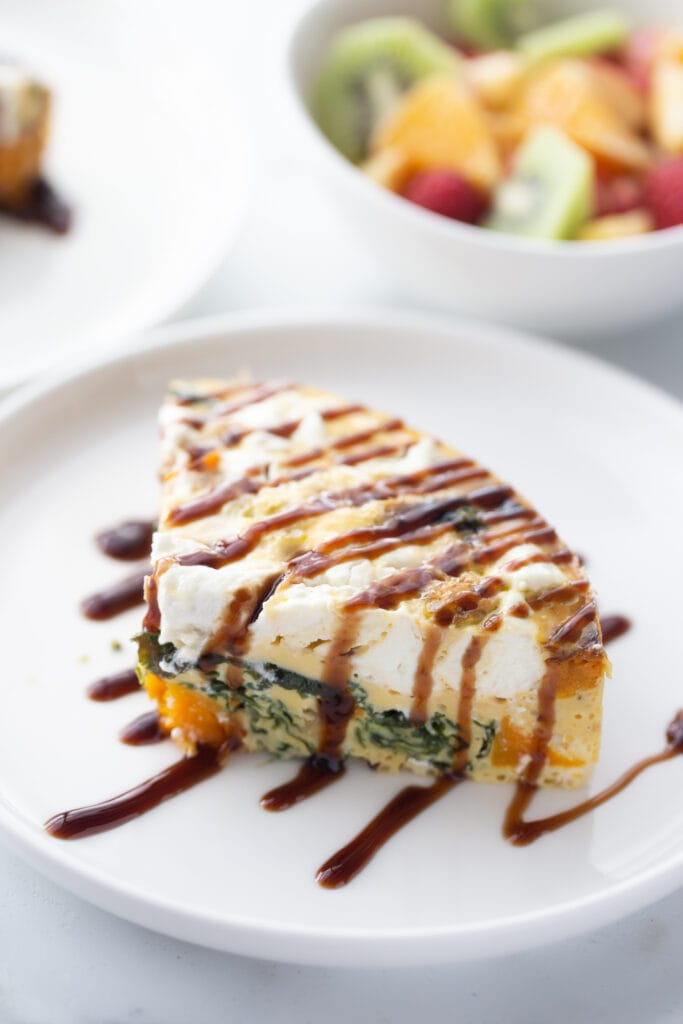 A slice of kale and butternut squash frittata on a white plate and topped with balsamic glaze.