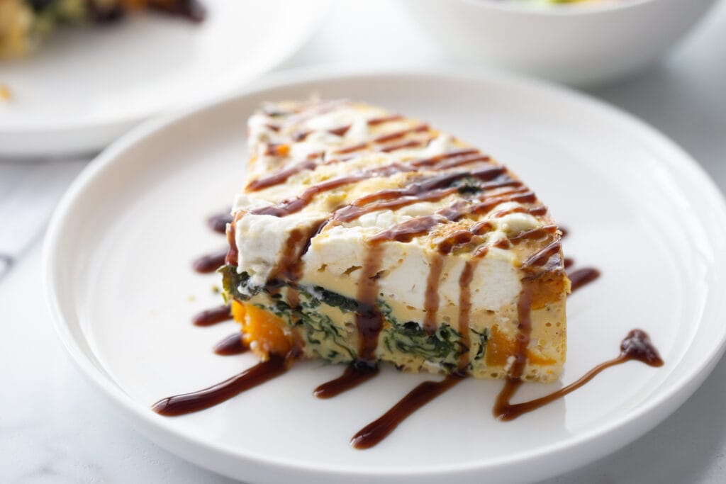 Landscape photo of a slice of frittata topped with goat cheese, drizzled with balsamic glaze.