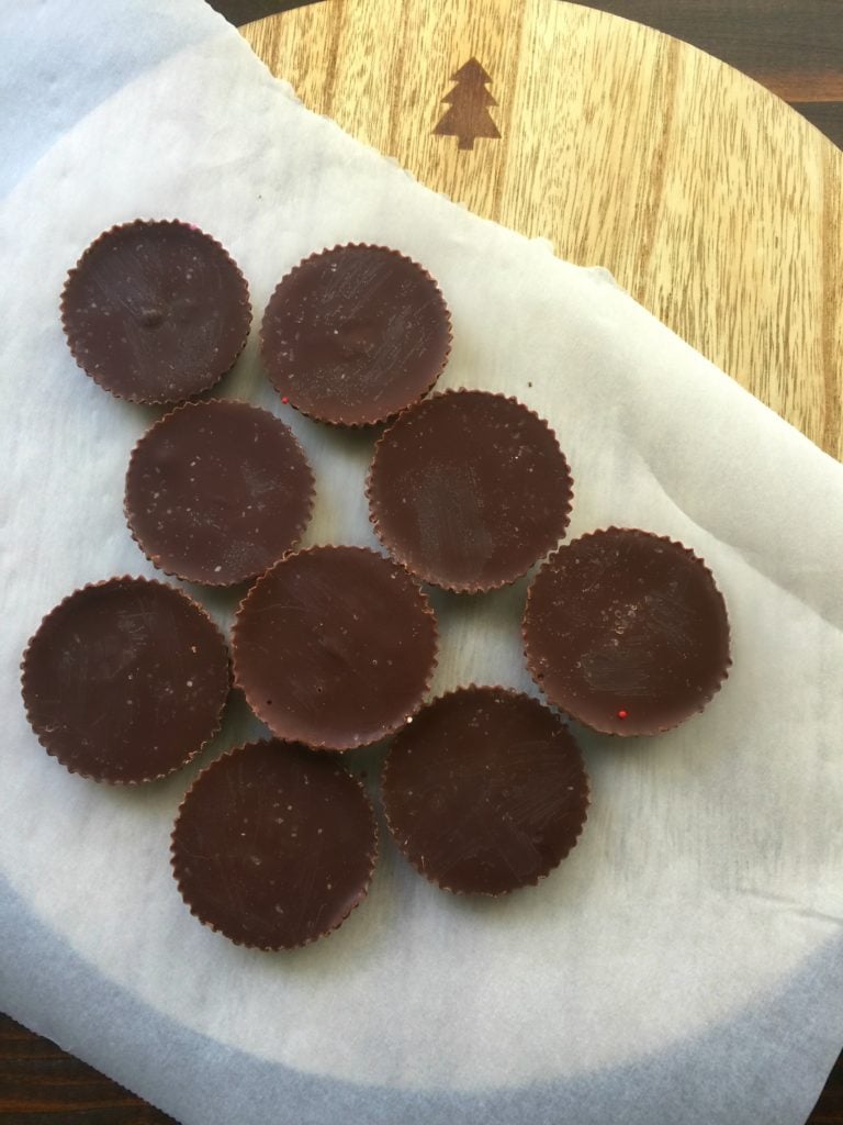 Chocolate peanut butter cup fudge circles on a piece of parchment paper on a wooden background.