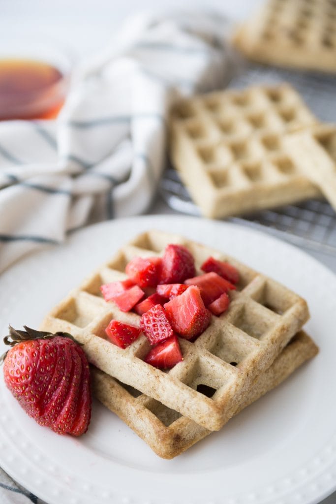 Two square homemade waffles on a white plate topped with diced strawberries and a sliced strawberry for garnish.