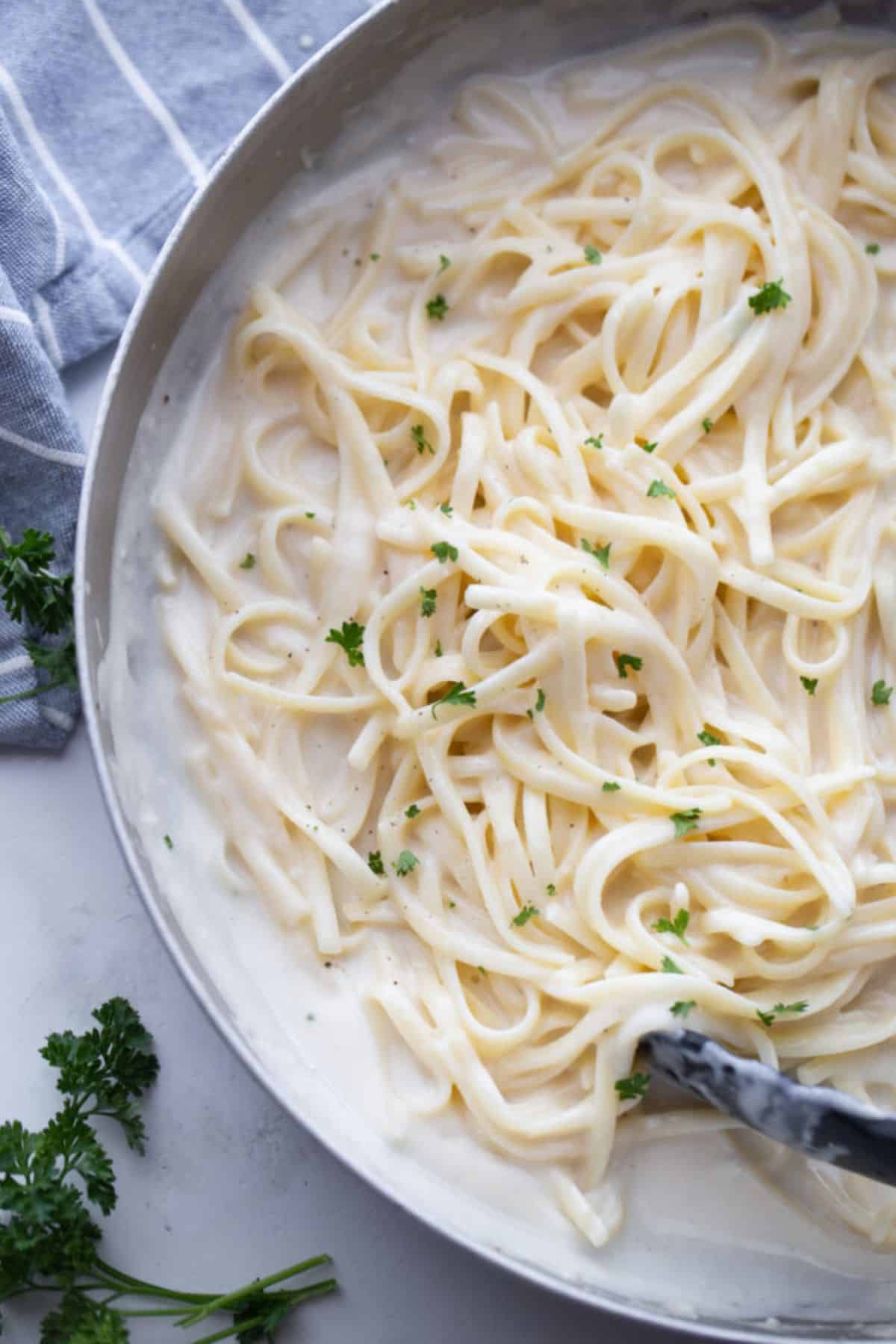 Healthier fettuccini alfredo in a stainless pan on a marble countertop.