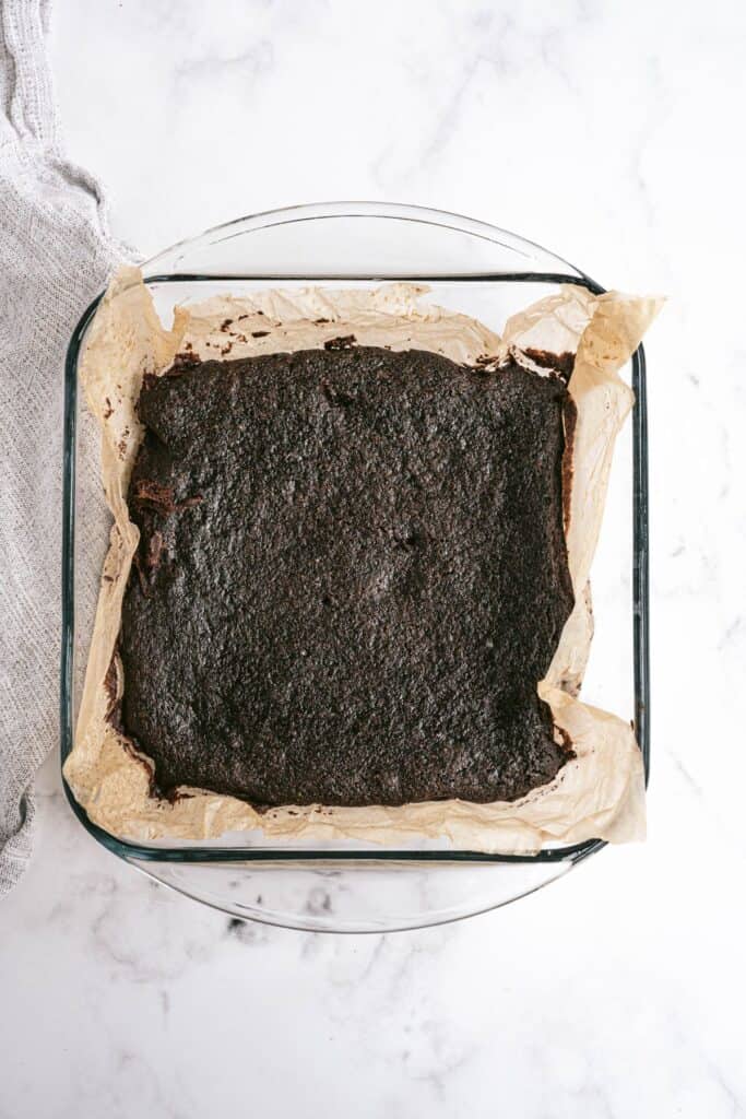 Glass pan lined with parchment paper with baked brownies.