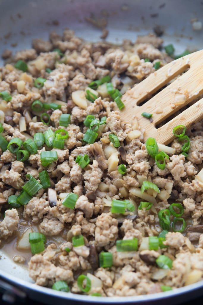 Ground chicken and veggies being sauteed in a pan with a slotted wooden spoon and garnished with green onions