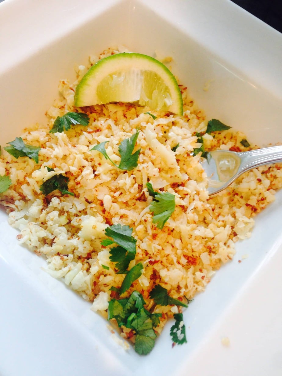 Cilantro lime cauliflower rice in a square bowl with a lime wedge and fork resting on the side