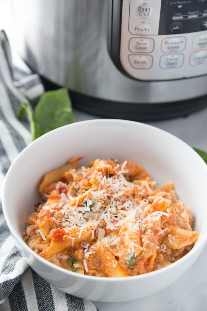White bowl of bake ziti topped with cheese with an Instant Pot in the background 