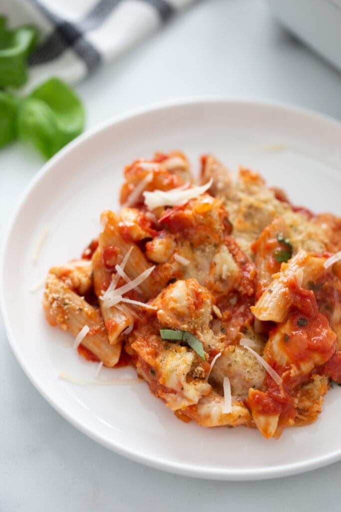 Penne pasta with tomato sauce, shredded cheese, and diced chicken piled high on a white plate.