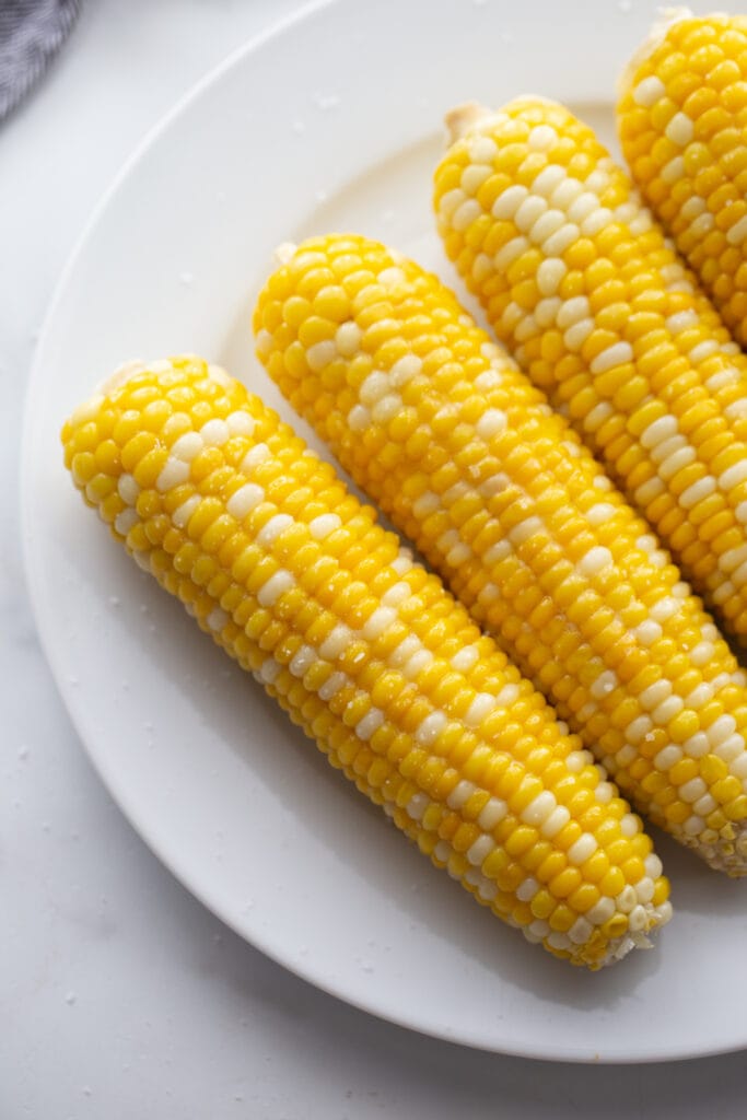 Overhead image: corn on the cob lined up on a white plate