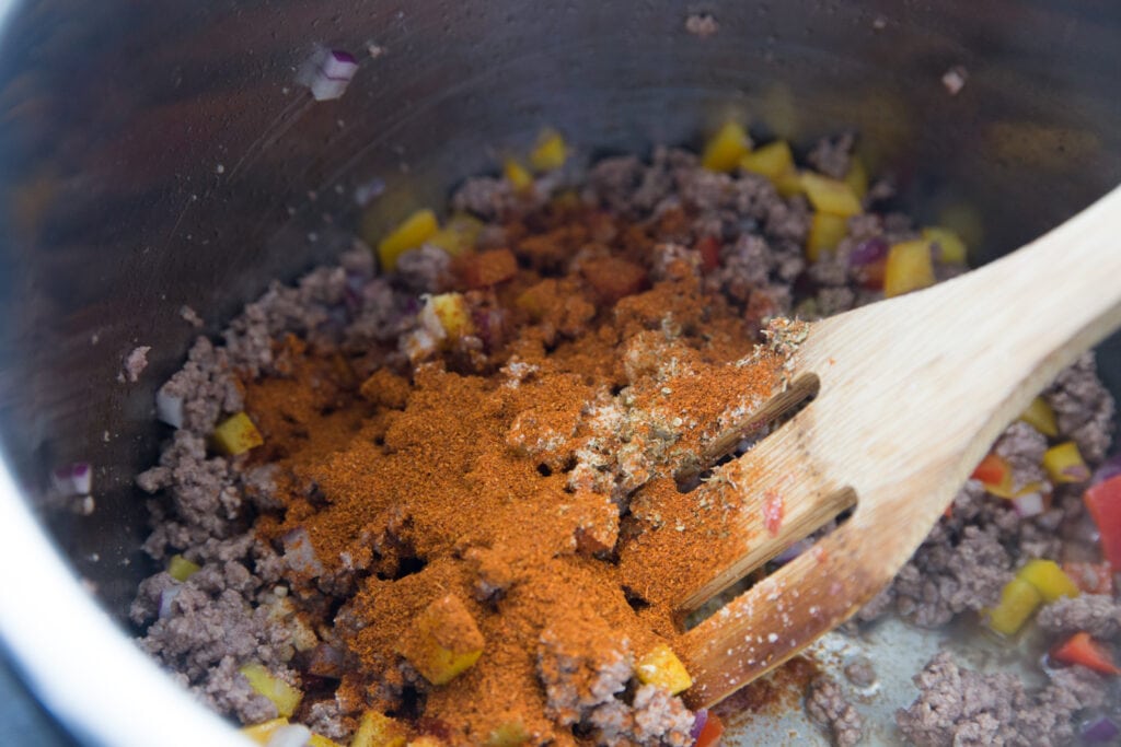 An Instant Pot with beef enchilada spices ready to be stirred with a wooden spoon