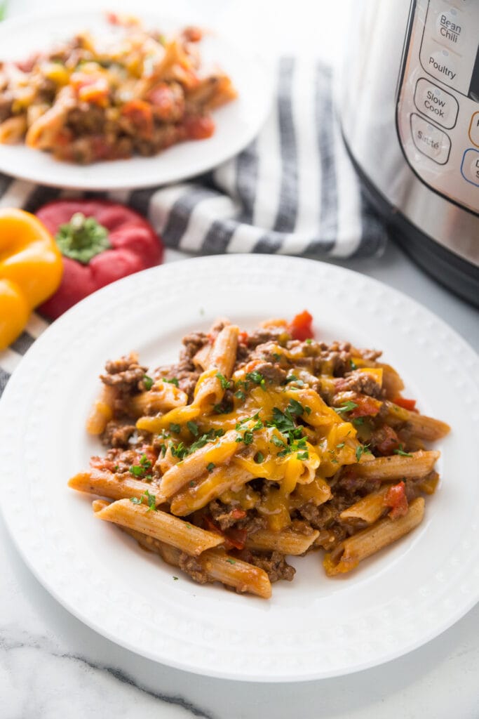 A plate of cheesy beef Instant Pot enchilada pasta with lots of veggies sitting next to an Instant Pot