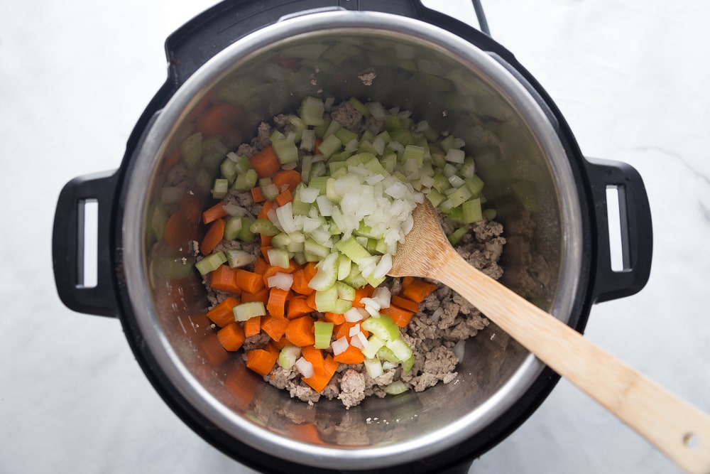 Instant Pot with carrots, celery, onion, ground turkey and a wooden spoon