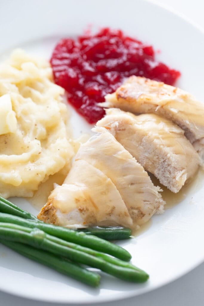 Close up photo of Instant Pot turkey breast topped with gravy on a plate with green beans, cranberry sauce, and mashed potatoes