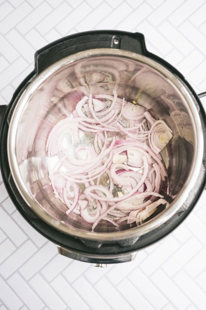 Overhead photo of red onion sauteing in the instant pot on a white tile surface.