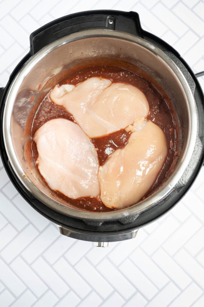 Overhead photo of an Instant Pot full of balsamic chicken ingredients, including chicken on the top.