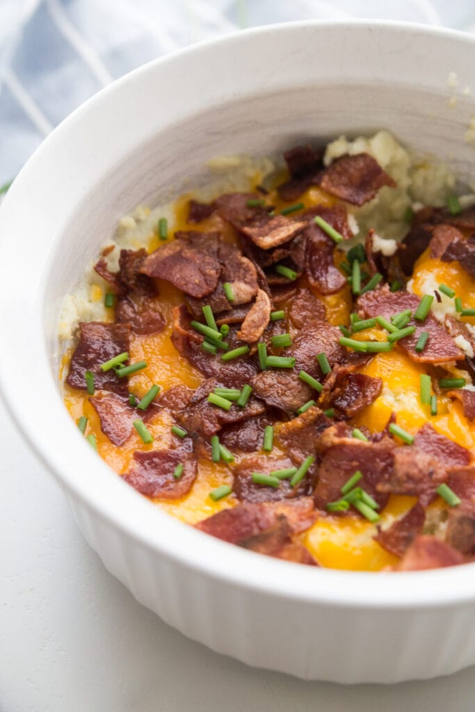 A white Instant Pot safe casserole dish topped with bacon, cheddar, and chives. 
