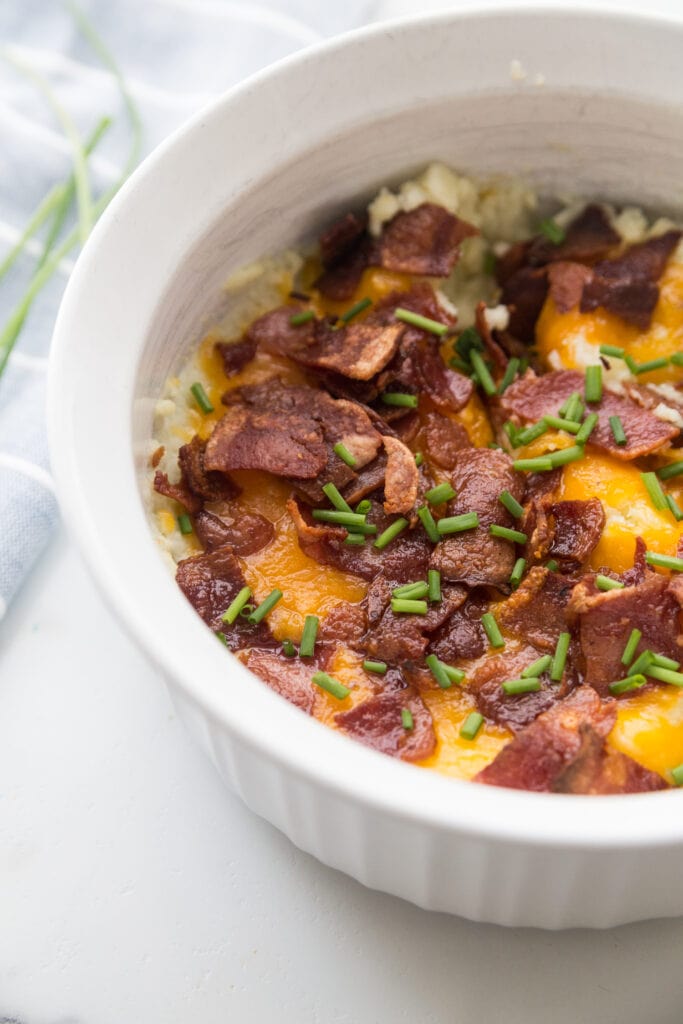 A white Instant Pot safe casserole dish with Mashed Cauliflower topped with bacon, cheddar, and chives. 