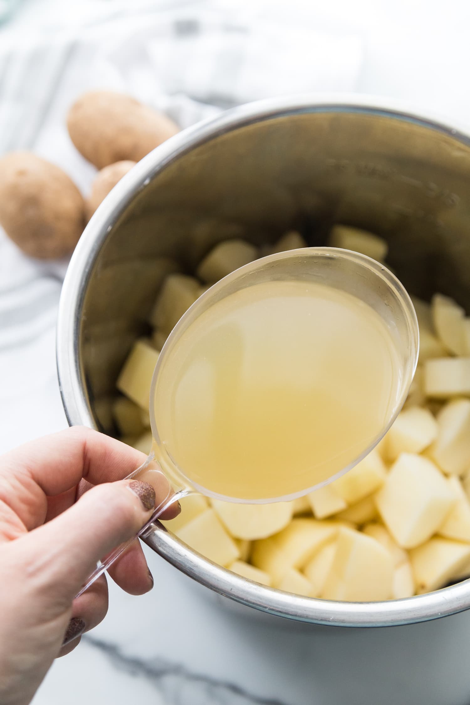 Photo of chicken broth in a measuring cup over a pot of diced potatoes for a dairy free instant pot mashed potatoes recipe.