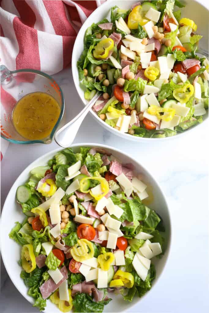 Two bowls of Italian Chopped Salad on a white backdrop with the dressing sitting nearby.