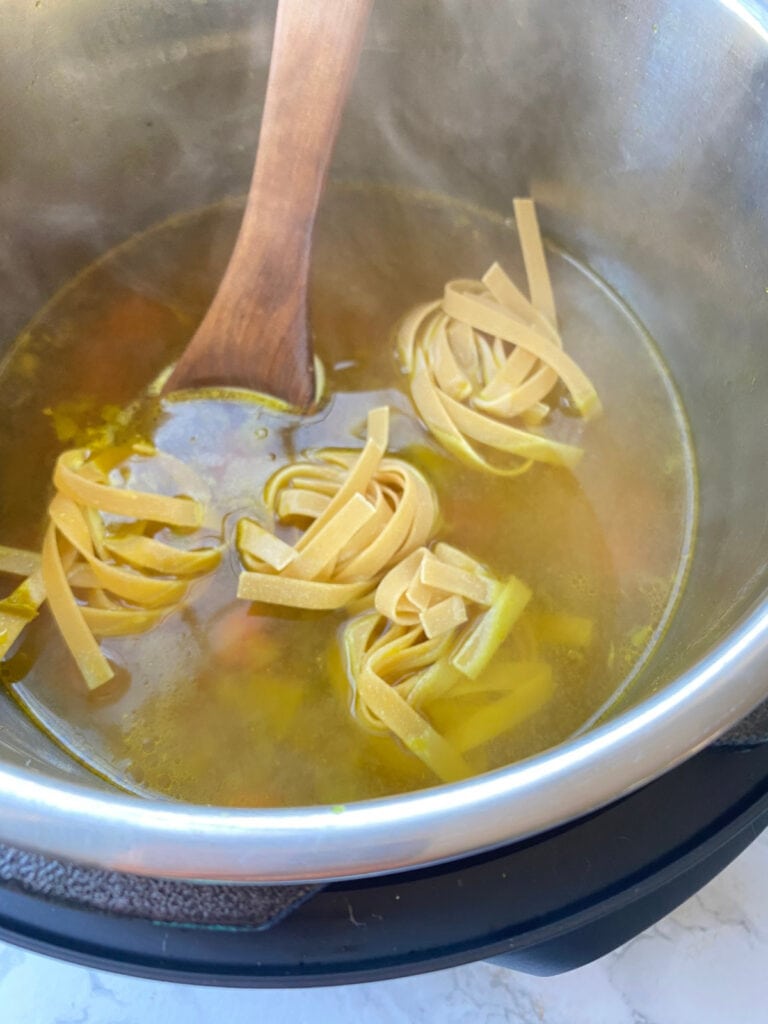 Egg noodles being cooked in soup broth in the Instant Pot for chicken noodle soup.
