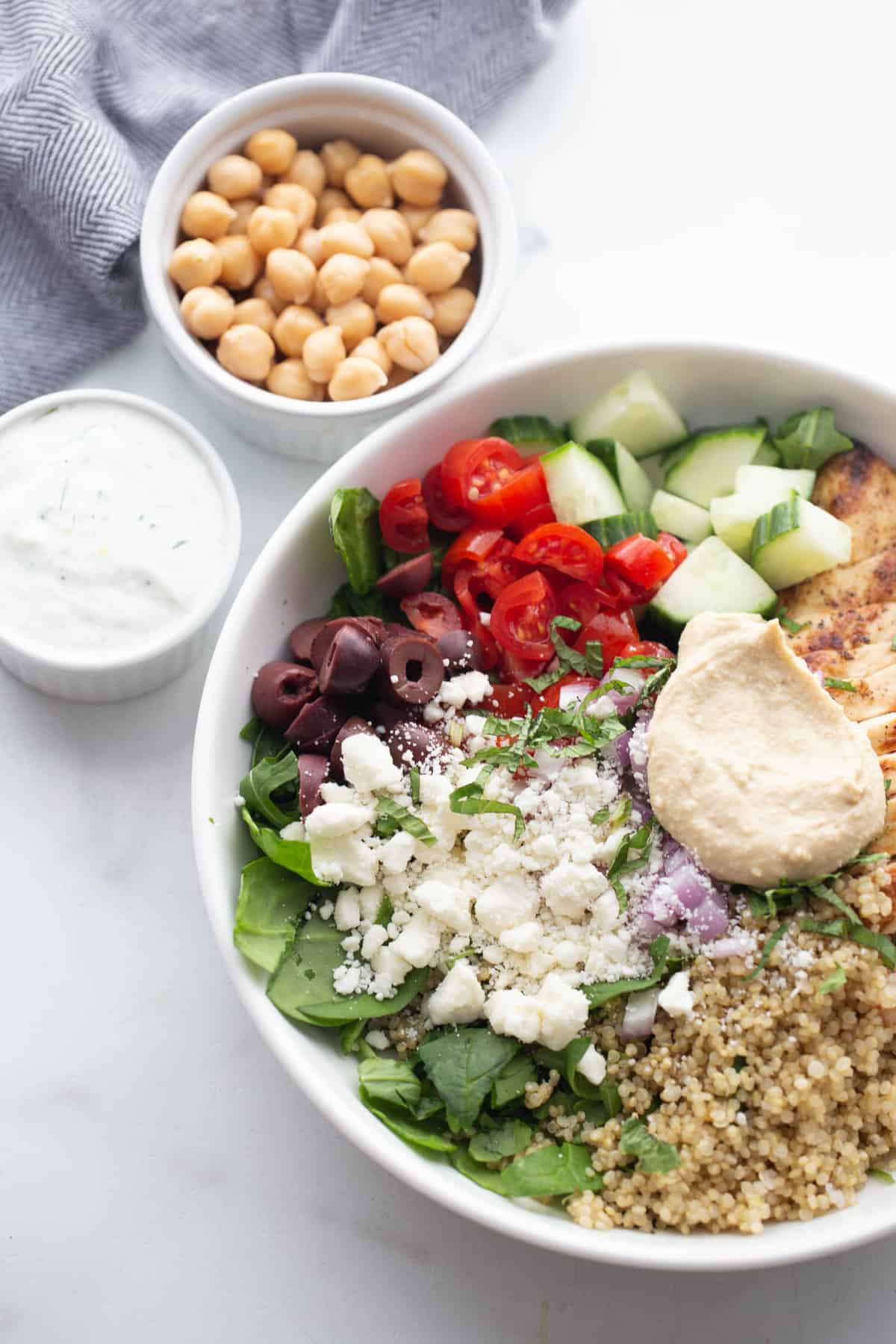 Mediterranean bowls with chicken and quinoa; tzatziki sauce and chickpeas are sitting next to the bowl.