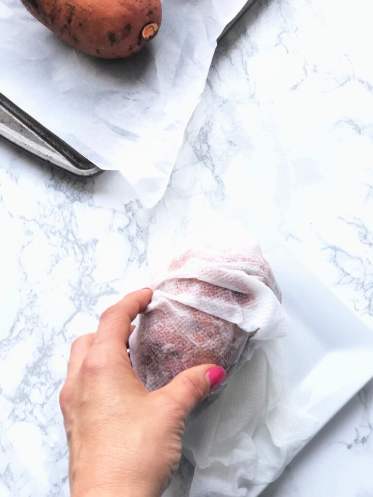 A sweet potato wrapped in a wet paper towel on a marble countertop