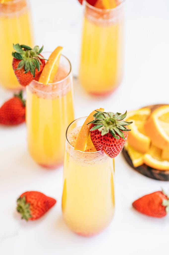 Champagne flutes with orange strawberry mimosas on a white table and a strawberry garnish 