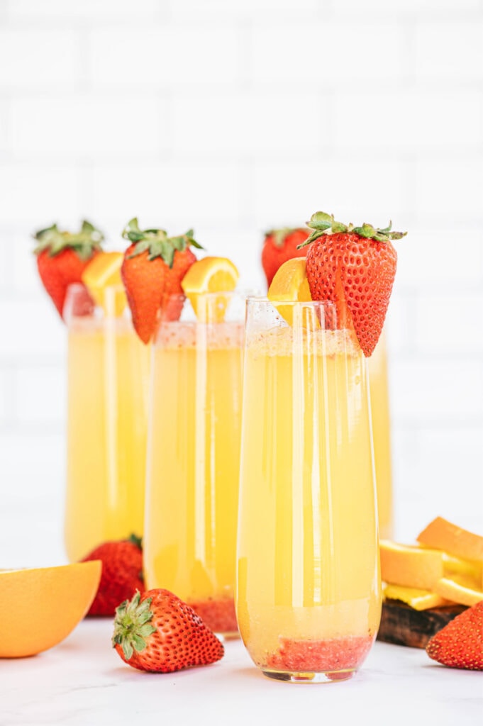 Champagne flutes with orange strawberry mimosas and a strawberry garnish 