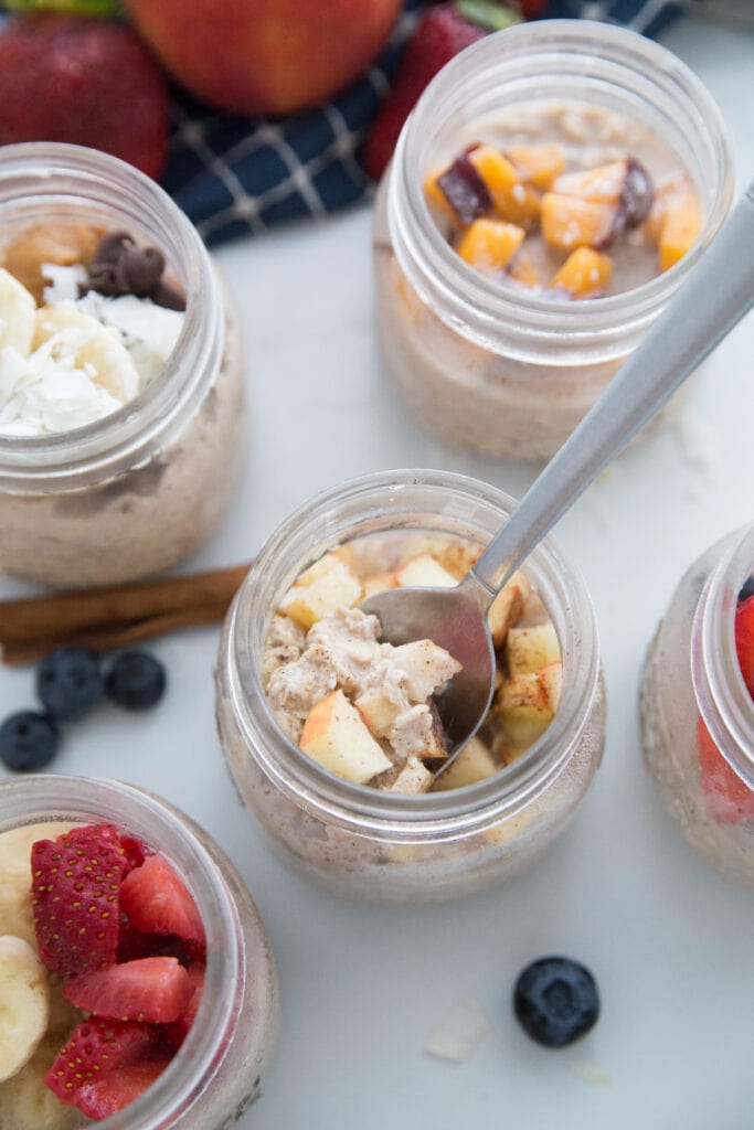 Overnight Oats in Mason Jars with 5 different toppings. The apple cinnamon one has a spoon inside.