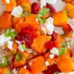 Sheet pan with roasted butternut squash and cranberries topped with goat cheese and fresh parsley and text for pinterest.